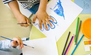 Manos de niños pintando, creando sus propios dibujos para imprimir. Lápices de colores y acuarelas a la vista.