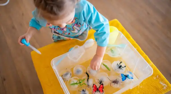 Niña haciendo experimentos para niños, liberando insectos de hielo con un gotero.