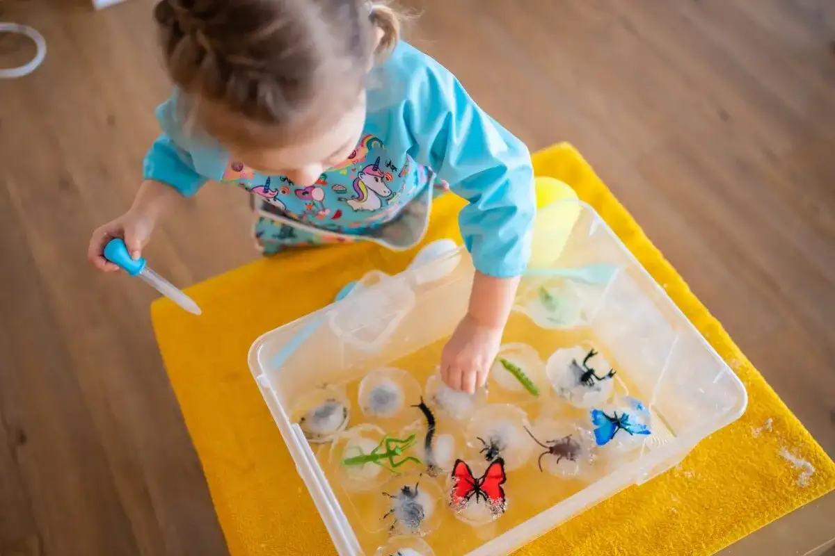 Niña haciendo experimentos para niños, liberando insectos de hielo con un gotero.
