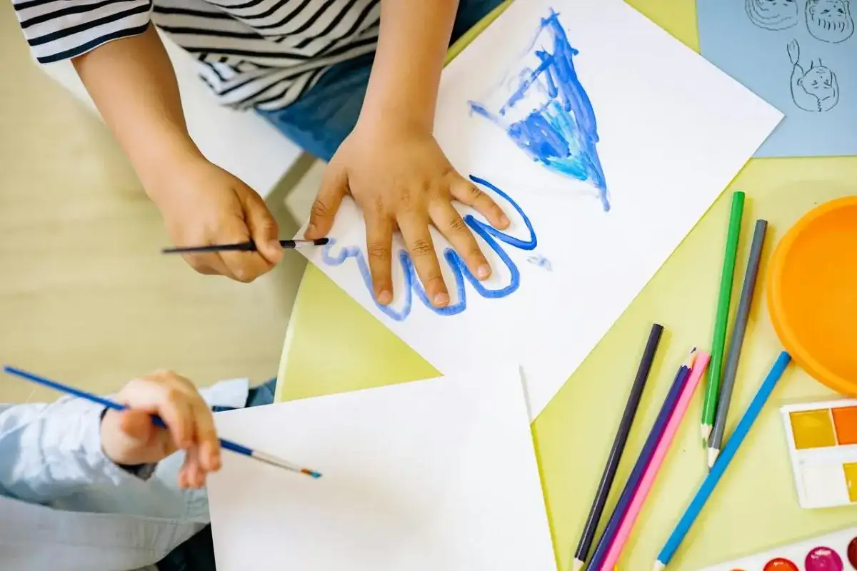 Manos de niños pintando, creando sus propios dibujos para imprimir. Lápices de colores y acuarelas a la vista.