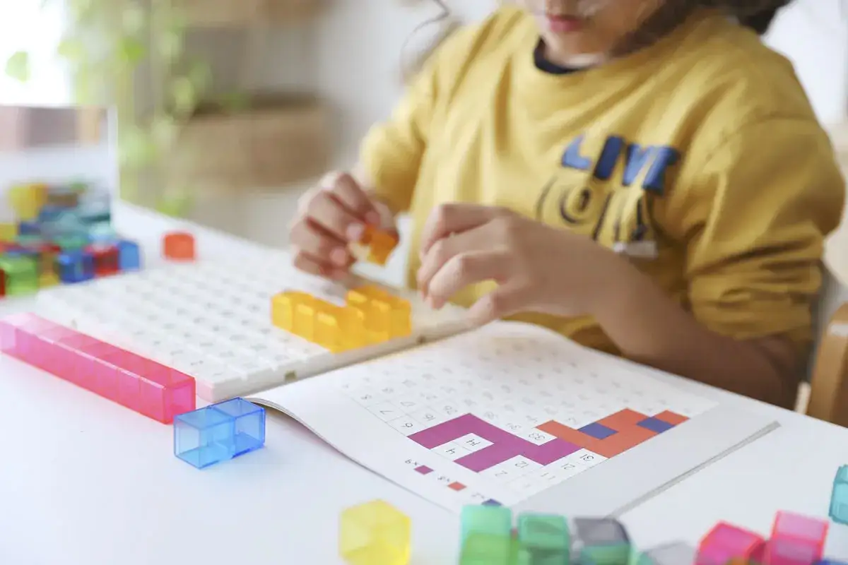 Ni&ntilde;a jugando con bloques de colores y un libro de juegos de matem&aacute;ticas.