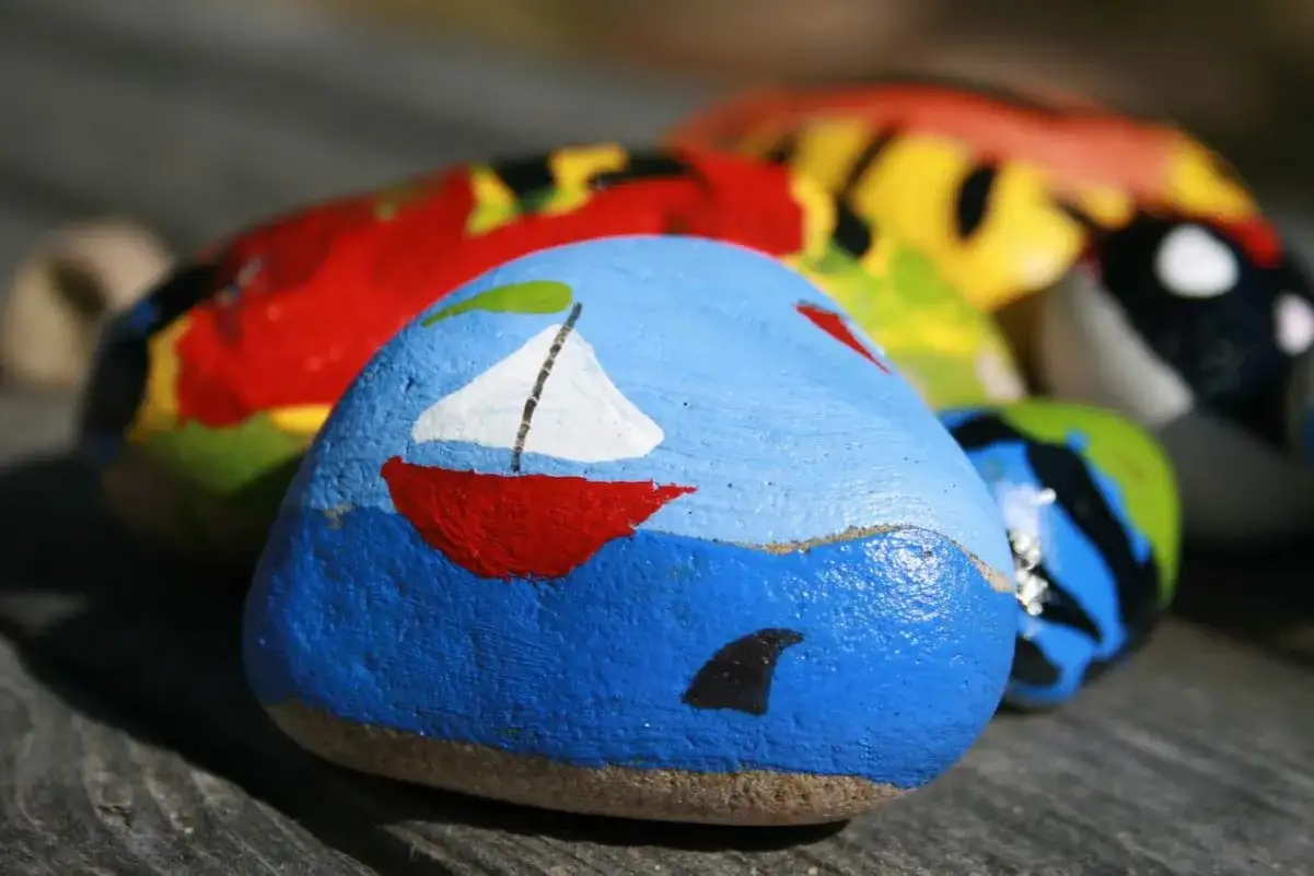 Piedras pintadas con ideas creativas: un barco rojo navega en mar azul con aleta de tiburón.