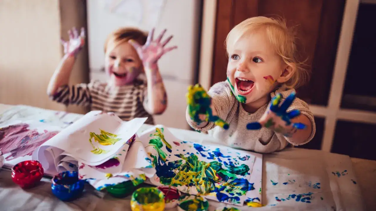 Ni&ntilde;os felices disfrutando de manualidades con pintura de dedos, sus manos y caras llenas de color.