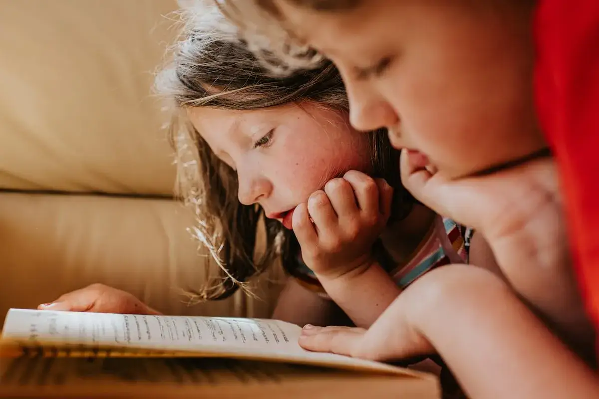 Dos ni&ntilde;os concentrados en un libro, aprendiendo a leer. Una escena tierna sobre como ense&ntilde;ar a leer a un ni&ntilde;o de 5 a&ntilde;os.