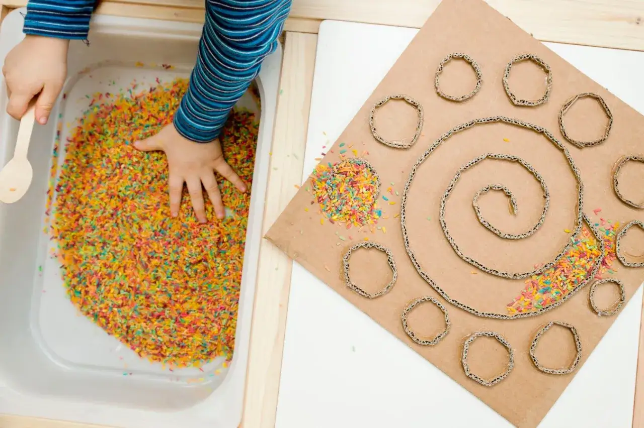 Ni&ntilde;o explorando diferentes tipos de texturas para ni&ntilde;os con arroz de colores y cart&oacute;n.