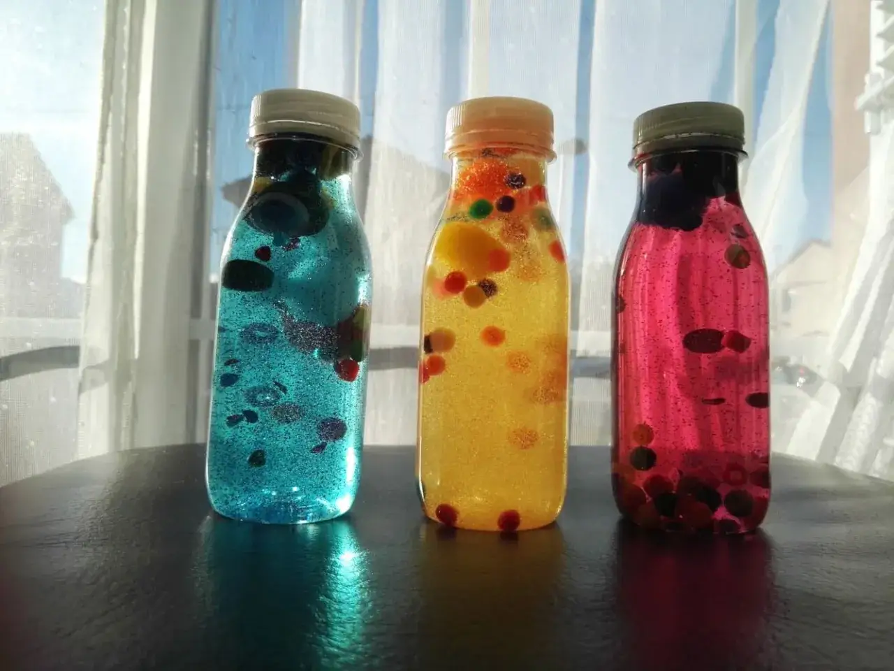 Tres botellas de plástico con líquidos de colores y brillos: azul, amarillo y rosa. Cada tarro de la calma contiene pequeñas bolitas y objetos flotantes, creando un efecto hipnótico.